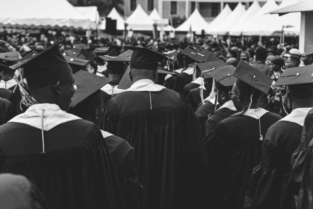 Black and white photo of students at a graduation ceremony, wearing gowns and caps.
